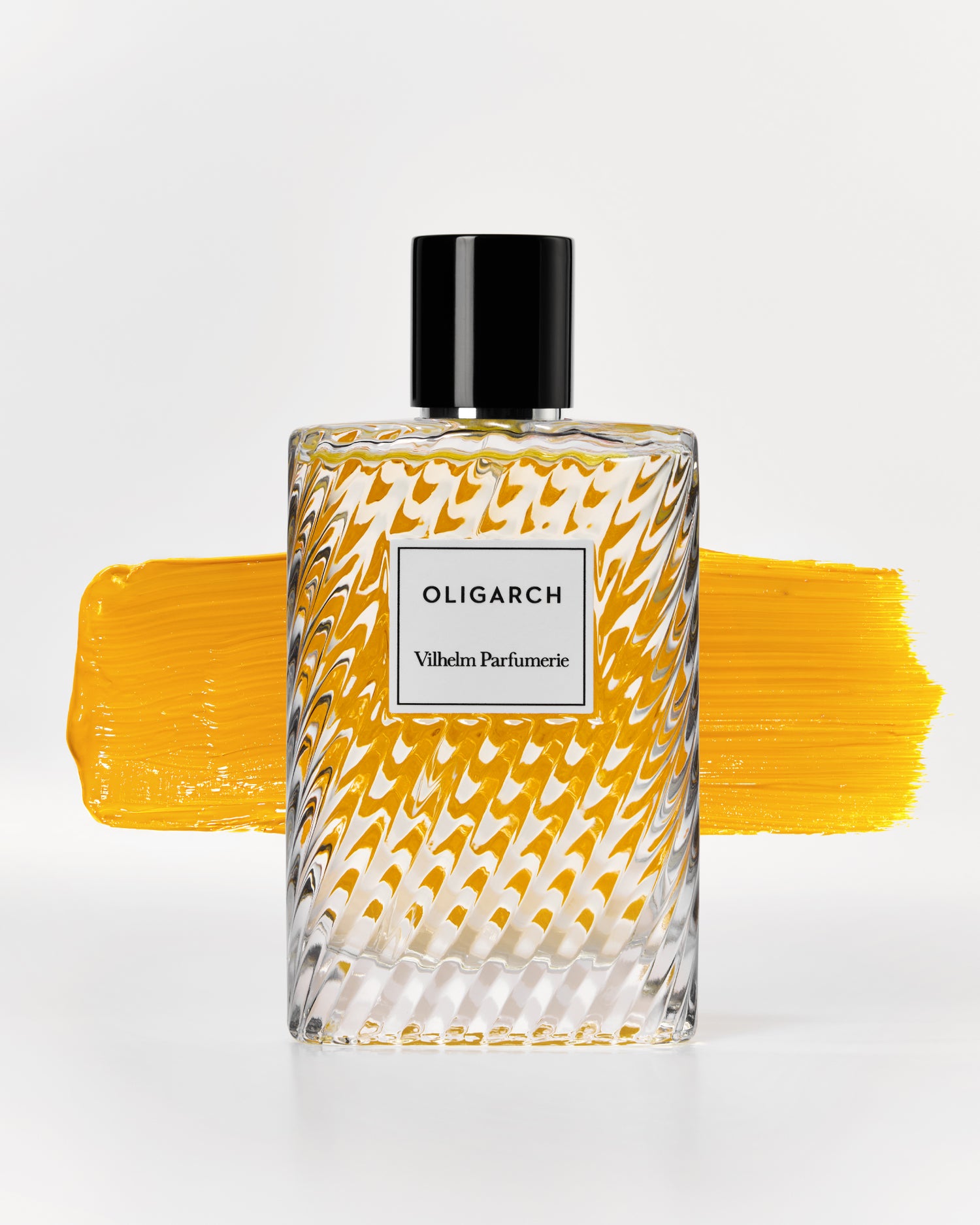 A clear glass perfume bottle with a black cap and a white label reading &